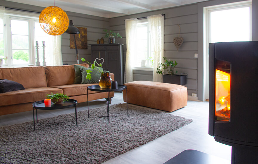 Piec na drewno w szarym salonie z drewnianymi ścianami i brązową sofą