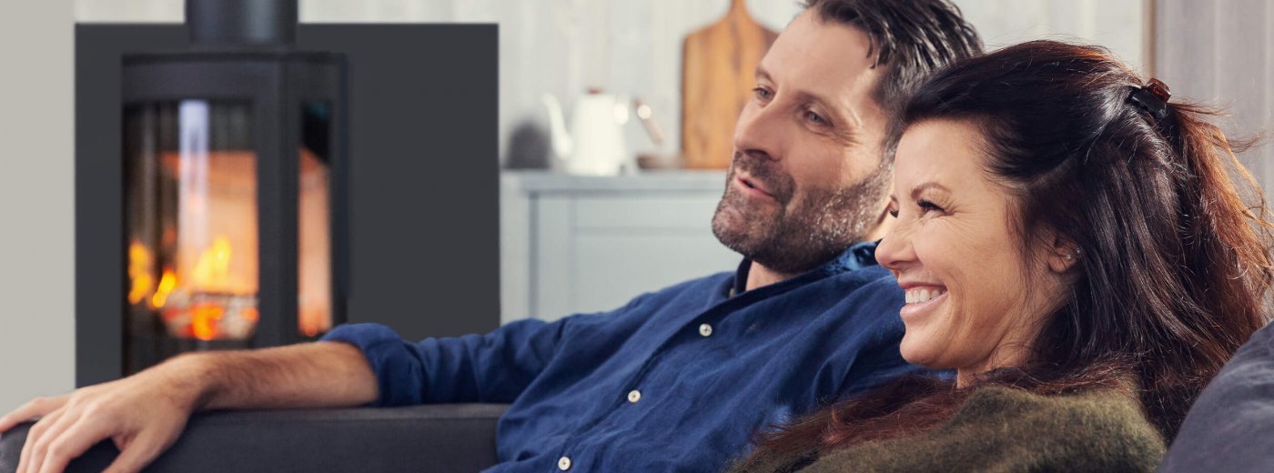 Mężczyzna i kobieta siedzą przed piecem opalanym drewnem Jøtul F 373 Advance w salonie