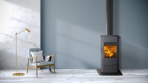 Czarny piec na drewno Jøtul F 232 w szarym pokoju z fotelem i lampą